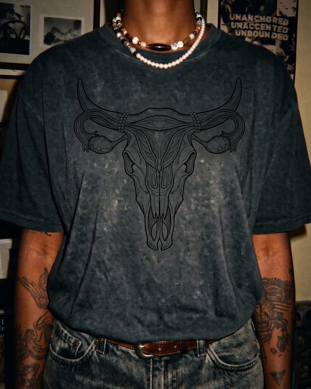 A charcoal acid-wash oversized tee printed in one black line with a female reproductive system — uterus, fallopian tubes and ovaries — drawn so the tubes sweep up into horns and the whole thing resolves into a longhorn skull